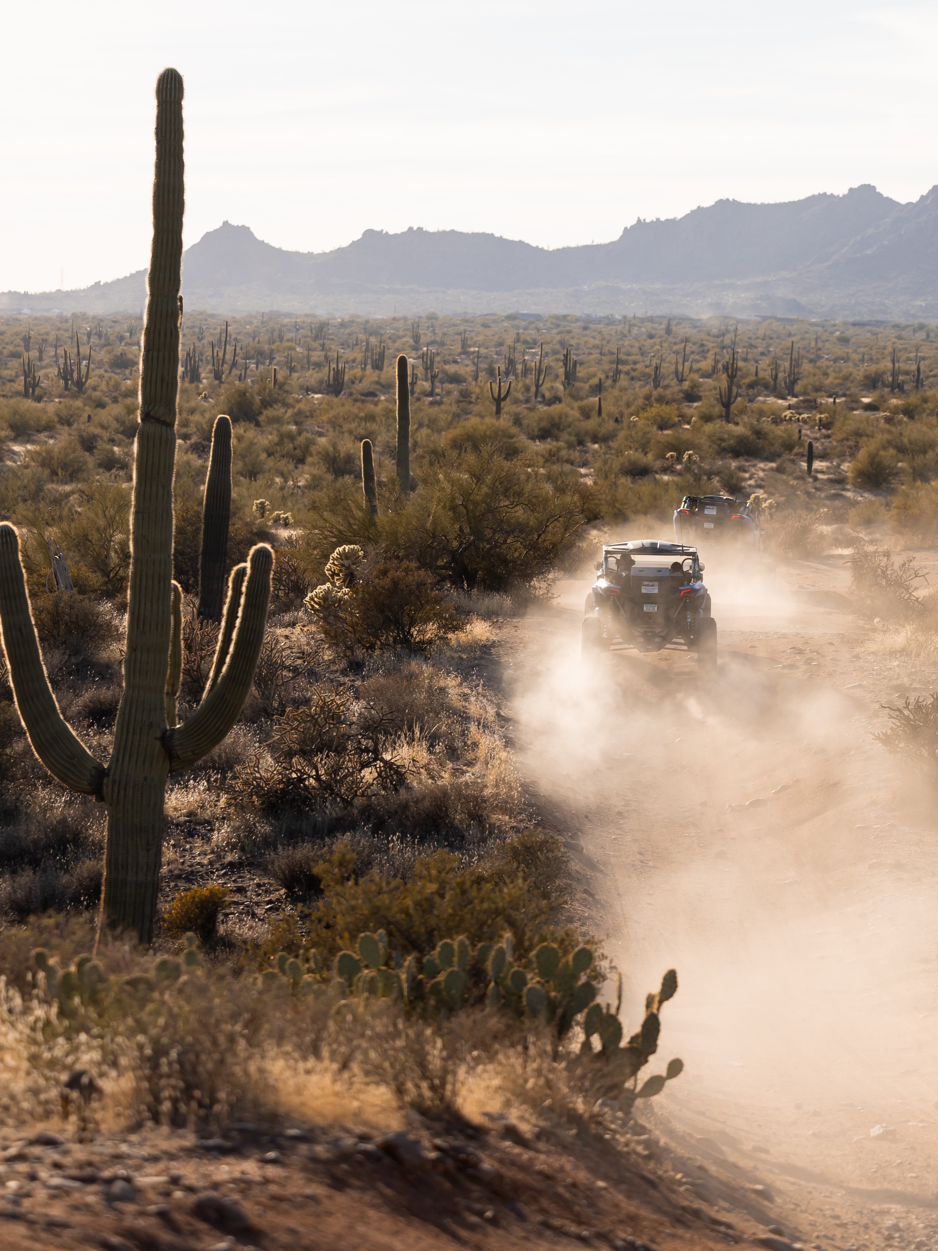 A dusty road with a car driving down it.